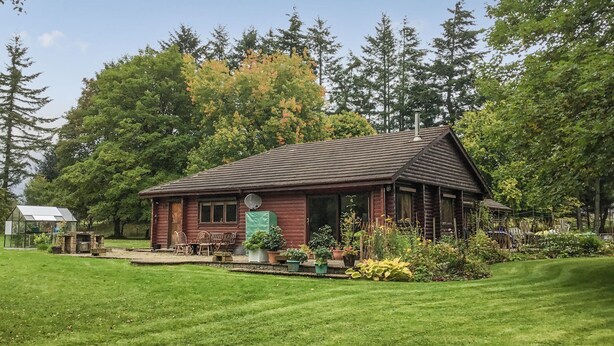 A log cabin with a sloped roof, surrounded by a well-maintained lawn and various potted plants. - 3 bedroom accommodation in Enochdhu, near Pitlochy (Enochdhu, near Pitlochy)