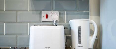 Una cocina con un tostador blanco, un hervidor eléctrico blanco y un enchufe en la pared con un interruptor rojo.