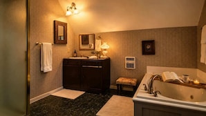 A bathroom with a dark marble floor, a large bathtub, a vanity with a mirror, a towel rack, and a wall-mounted light fixture. - Bailey Inglish Suite • Private Balcony (Bonham)