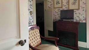 A room with floral wallpaper, a wooden chair, a television on a stand, and a door. - Bailey Inglish Suite • Private Balcony (Bonham)