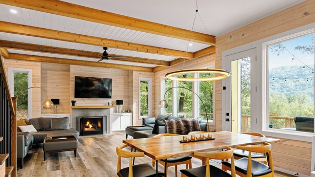 Un vaste espace de vie doté d’un plancher en bois, d’une cheminée, d’un grand téléviseur et d’une table à manger avec des chaises.