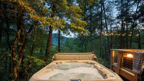 Un bain à remous situé dans un espace boisé, avec un chalet en bois et des guirlandes lumineuses.