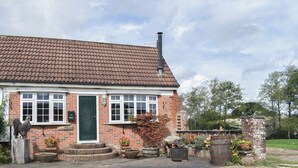 A brick house with a tiled roof, a green door, and a small front garden with potted plants and a wooden barrel. - The Coach House - UK41070 (Wootton, near Ryde)