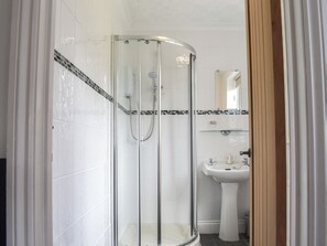 Eine Dusche mit Glastür, ein Waschbecken mit Spiegel darüber und eine geflieste Wand mit dekorativer Bordüre.