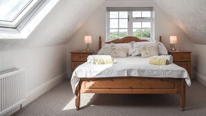 A bedroom with a sloped ceiling, a skylight, a large window, a wooden bed, two bedside tables, and a radiator. - The Coach House - UK41070 (Wootton, near Ryde)