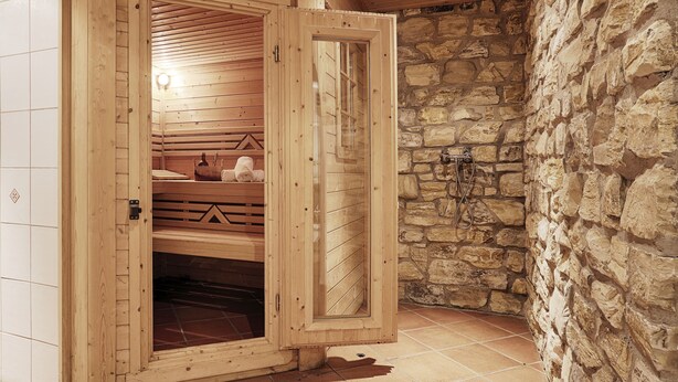 A sauna with wooden walls and a stone wall. - Landhotel Schwab Ferienhaus (Schwarzach am Main)