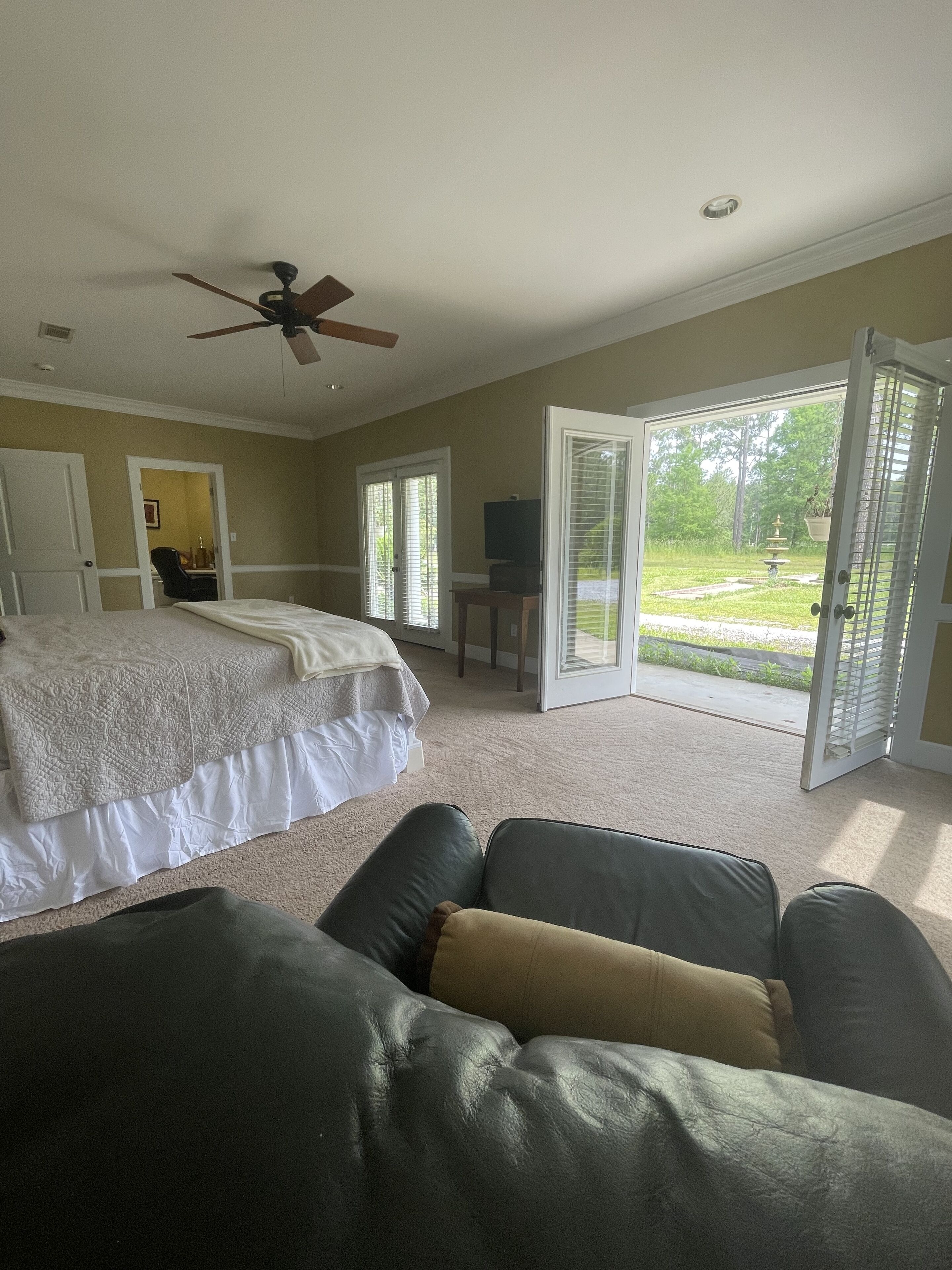 A bedroom with a bed, a ceiling fan, a TV, and a sliding glass door to a garden.