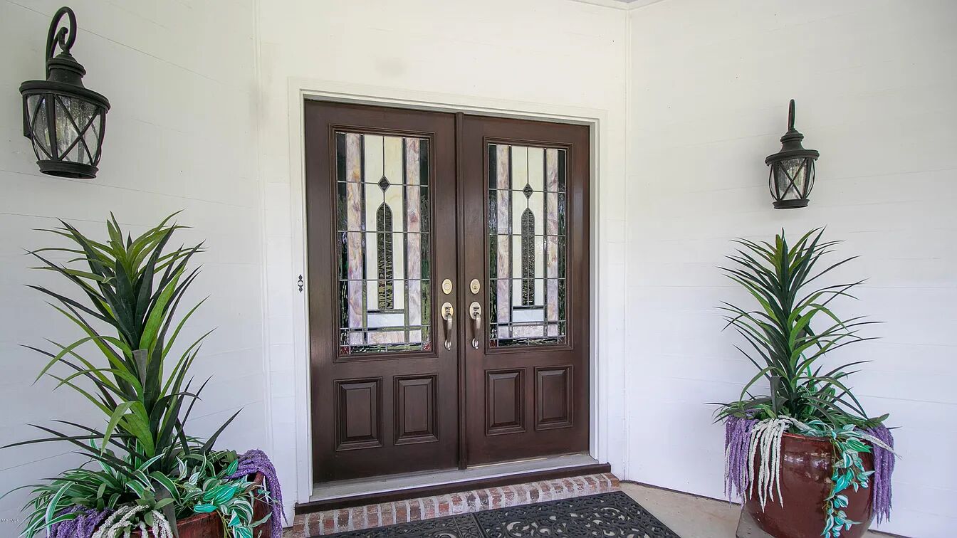 A double wooden door with glass panels, flanked by two potted plants with trailing vines.