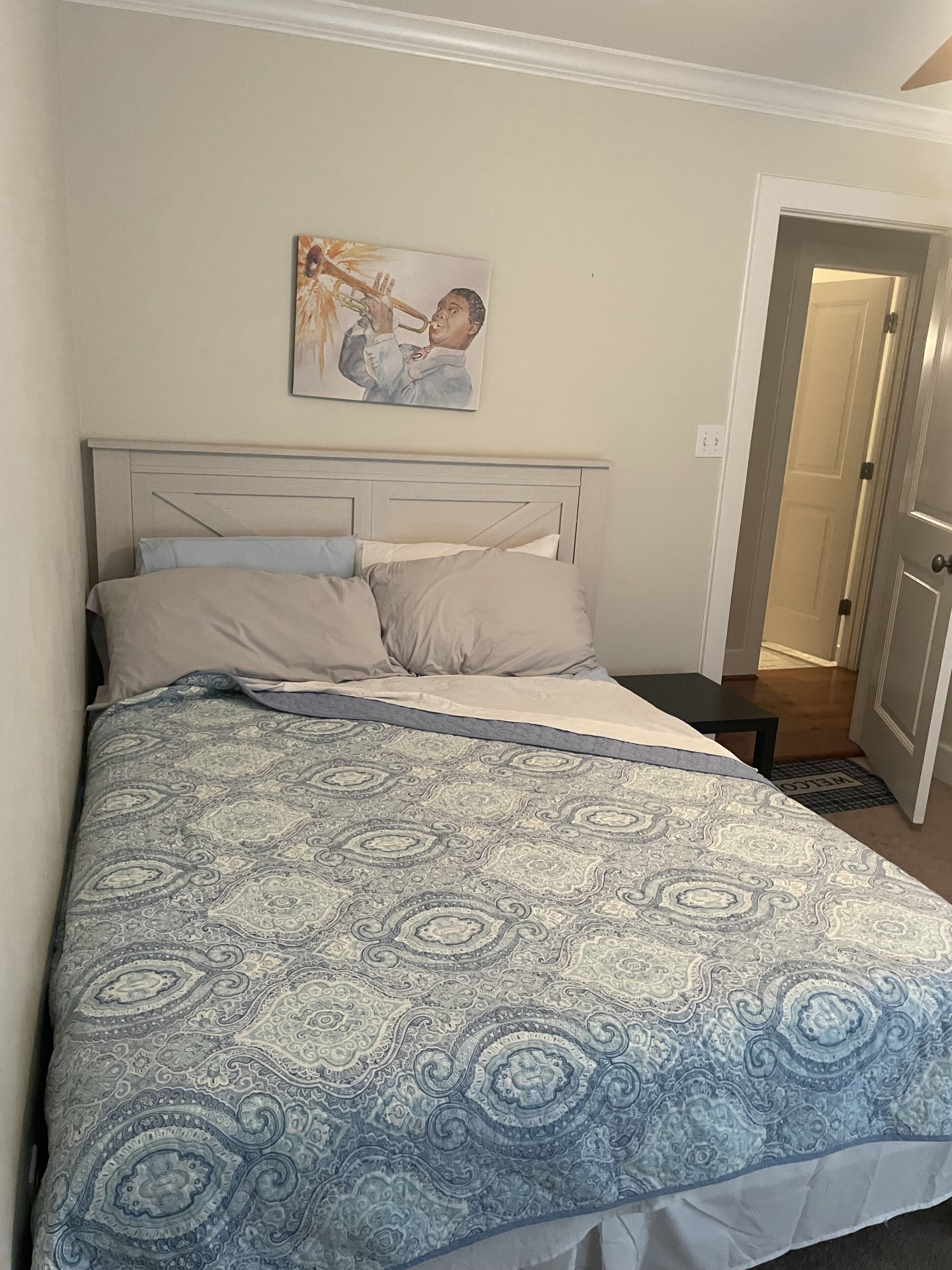 Ein Schlafzimmer mit einem Bett, einem Kopfteil, einem Gemälde und einer Tür.