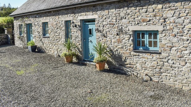 A stone building with a blue door and windows, surrounded by gravel and potted plants. - Ysgubor Blaenparc Barn - UK41030 (Dihewyd<br />, near Aberaeron)
