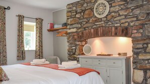 A bedroom with a stone wall, a bed with white linens, a dresser, and a mirror. - Ysgubor Blaenparc Barn - UK41030 (Dihewyd<br />, near Aberaeron)