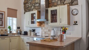 A kitchen with stone wall accents, white cabinetry, a central island, and a clock on the wall. - Ysgubor Blaenparc Barn - UK41030 (Dihewyd<br />, near Aberaeron)