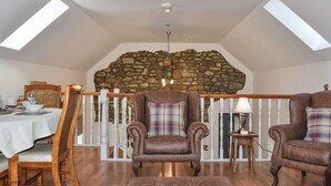 A spacious loft with a high ceiling, stone wall, wooden floor, and a dining area with a table set for two. - Ysgubor Blaenparc Barn - UK41030 (Dihewyd<br />, near Aberaeron)