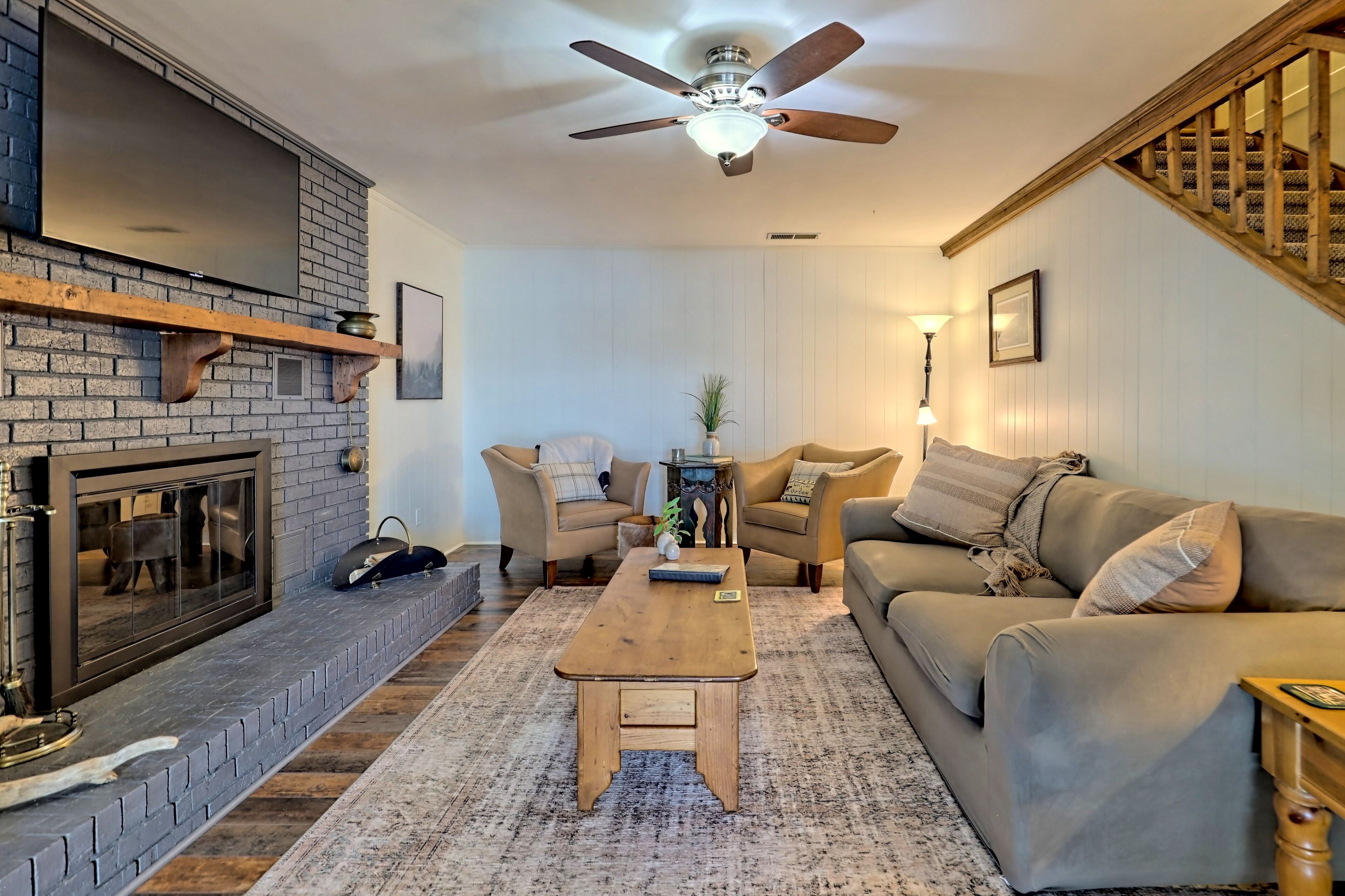 A cozy living room with a fireplace, a ceiling fan, a sofa, and a coffee table.