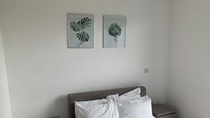 A bedroom with a bed, two nightstands, and two framed botanical prints on the wall. - Luxury 2-Bed High-rise Apartment with beautiful view near Excel, &O2. Next to CR (London)