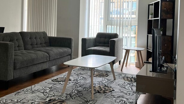 A modern living room with a grey sofa, a white coffee table, and a patterned rug. - Luxury 2-Bed High-rise Apartment with beautiful view near Excel, &O2. Next to CR (London)