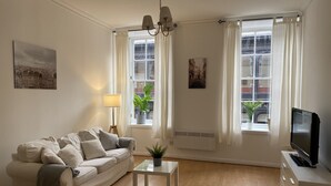 A living room with a sofa, a coffee table, a TV, and two windows with curtains. - Lovely 1-bed Apartment in Glasgow Merchant City (Glasgow)