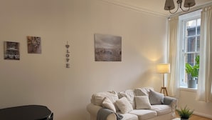 A living room with a white sofa, a small table, a black chair, and a window with curtains. - Lovely 1-bed Apartment in Glasgow Merchant City (Glasgow)