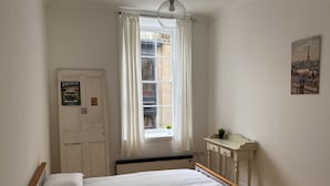 A bedroom with a bed, a window with curtains, a door with a sign, a small table with a plant, and a cityscape painting on the wall. - Lovely 1-bed Apartment in Glasgow Merchant City (Glasgow)