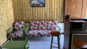 A cozy room with wooden walls, a floral sofa, a small table, and a green bench. - Studio 40 m2 (les trois ilets, le marin)