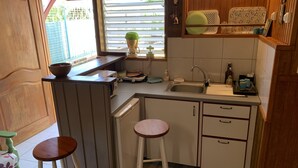 A compact kitchen with a sink, a microwave, a small refrigerator, and two stools. - Studio 40 m2 (les trois ilets, le marin)