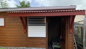A wooden house with a red roof, a window with white shutters, and a green chair inside. - Studio 40 m2 (les trois ilets, le marin)