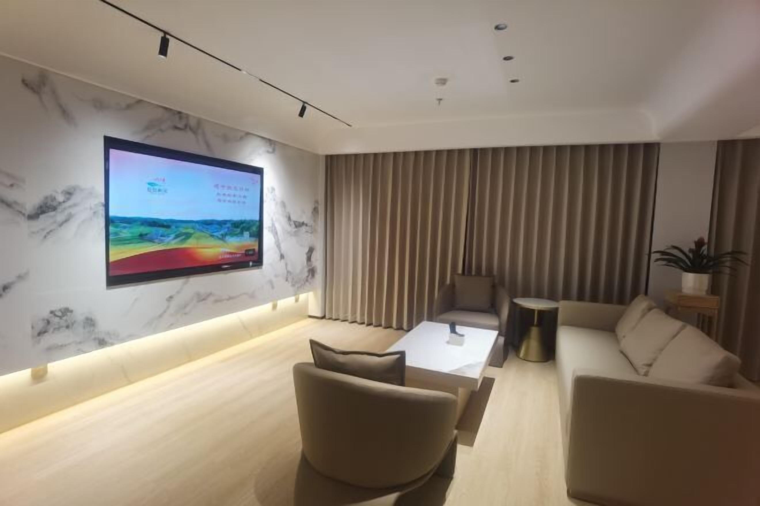 Una sala moderna con un televisor de pantalla plana grande montado en una pared de mármol, un sofá color beige, una mesa de centro y una cortina a rayas.