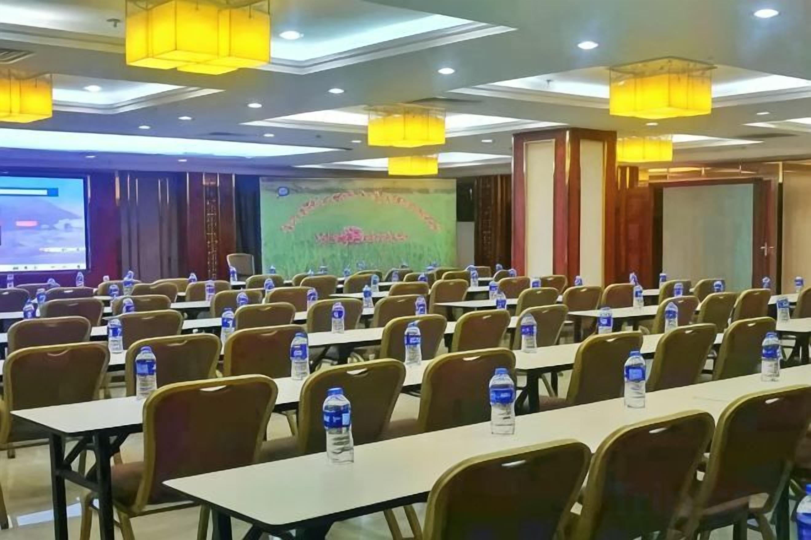 Un salón de conferencias con filas de mesas, sillas y botellas de agua.
