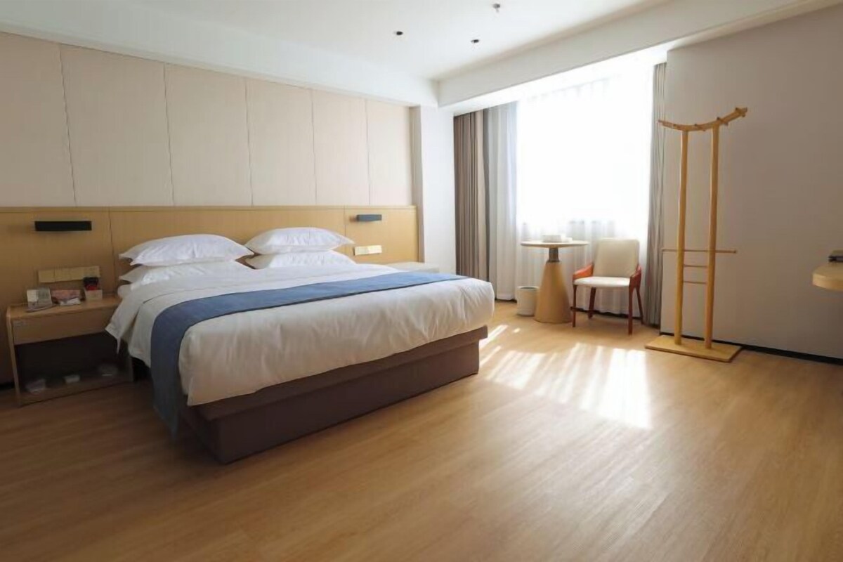 A modern hotel room with a large bed, bedside tables, a small desk, and a chair.