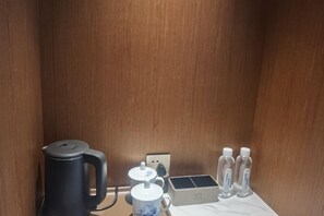 A small wooden cabinet with a black electric kettle, a white mug, a small box, and two water bottles. - Lotus Hotel (Jianning)