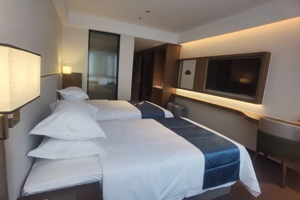 A hotel room with two beds, a large mirror, a flat-screen TV, and a desk with a chair.