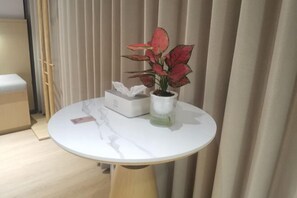 A round table with a white surface, a potted plant, a tissue box, and a glass container.