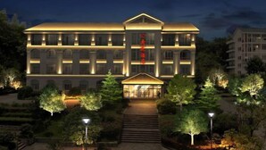 A multi-story hotel with a central entrance, surrounded by landscaped gardens and trees.