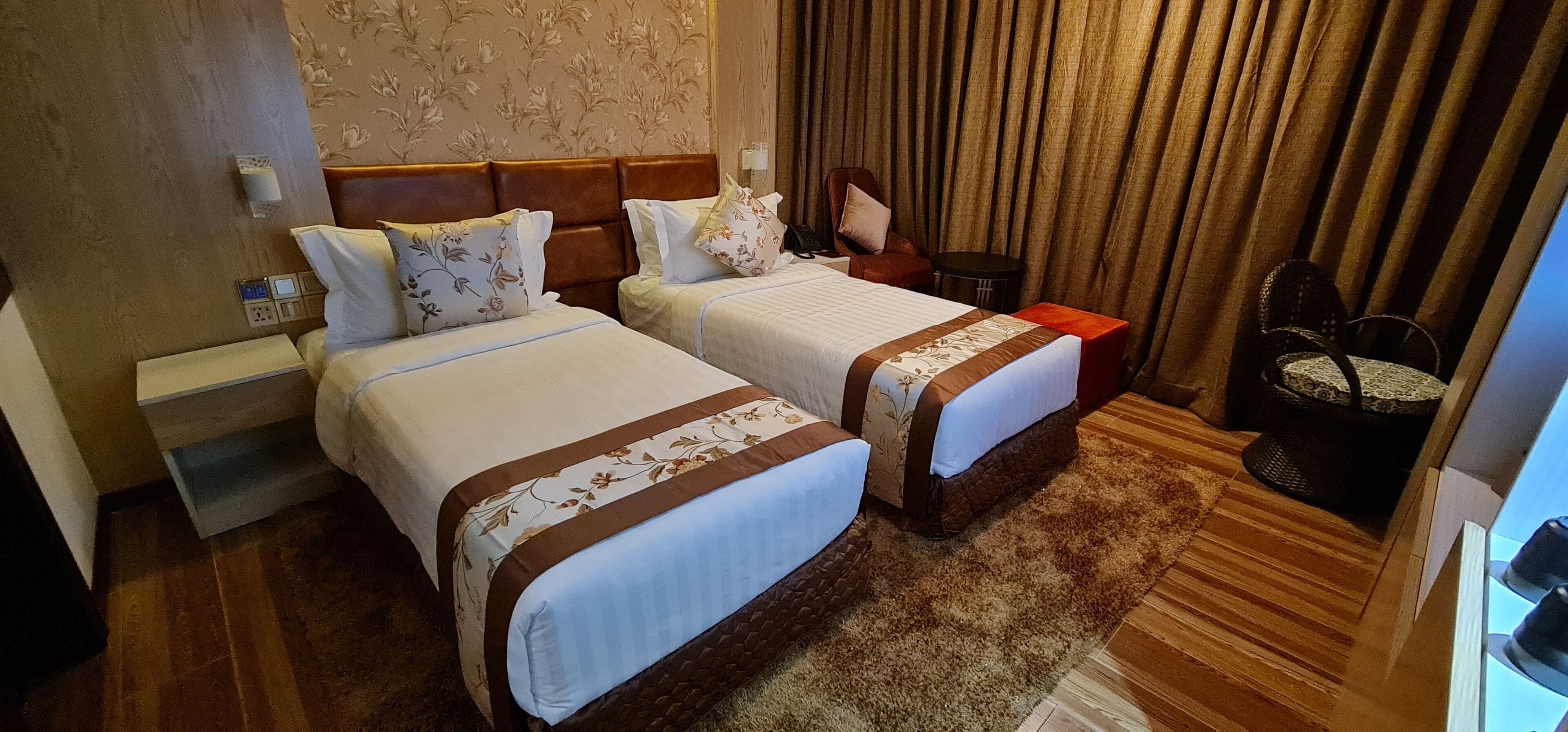 Une chambre d’hôtel avec deux lits, une table de chevet, une petite table, une chaise et un rideau.