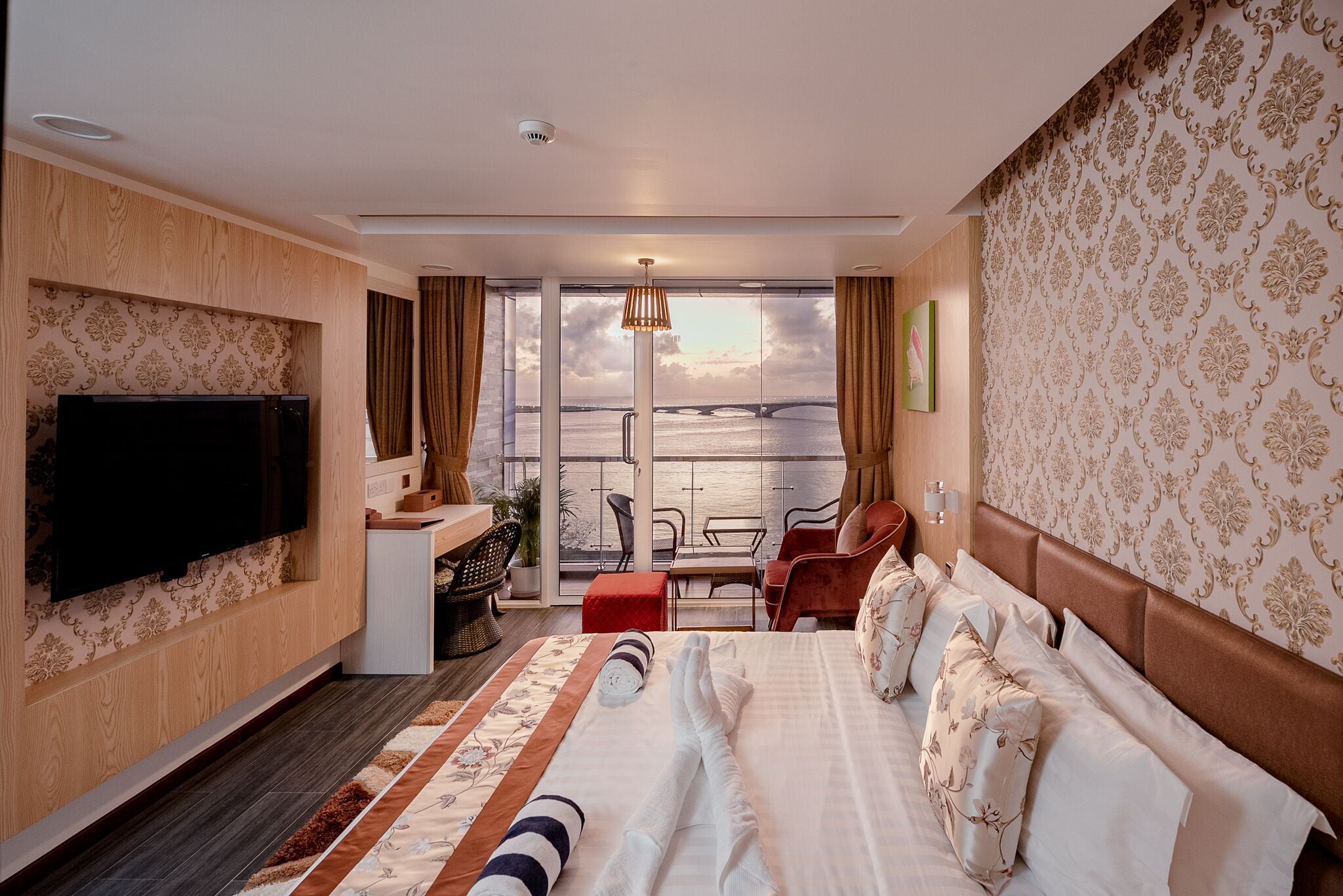 Une chambre d’hôtel avec un grand lit, un bureau avec une chaise, une télévision et une vue sur un pont et sur l’eau.