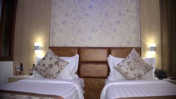 A hotel room with two beds, a wooden headboard, floral wallpaper, bedside lamps, and a nightstand with a telephone and a clock.