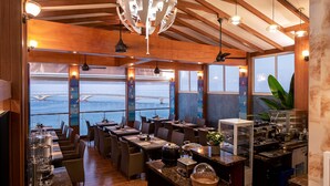 A restaurant with wooden beams, large windows, and a view of a bridge. Tables are set with glasses and cutlery. - Summer Beach Maldives (Malé)