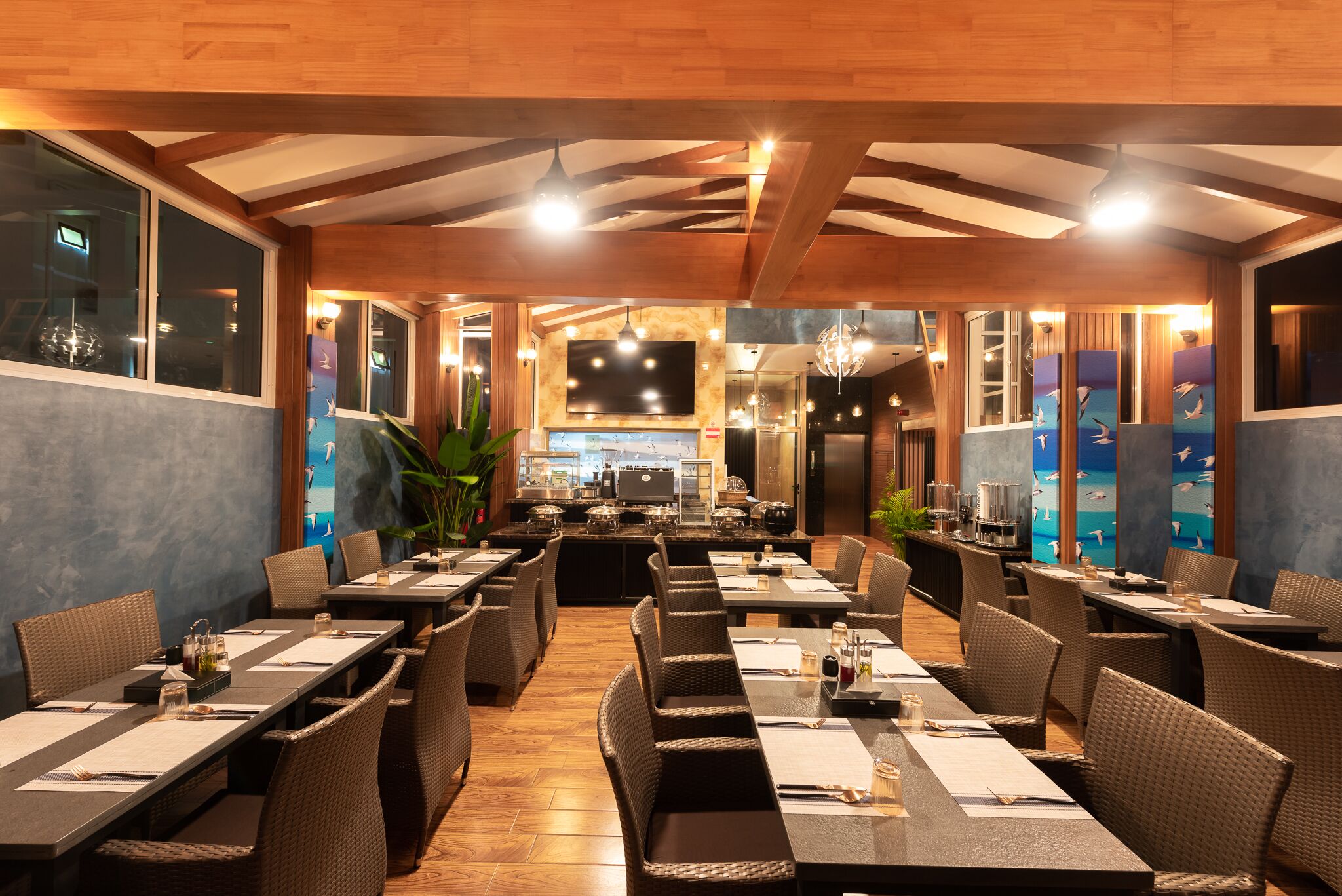 Un restaurante con mesas largas, sillas de mimbre y una zona de bar en el centro.