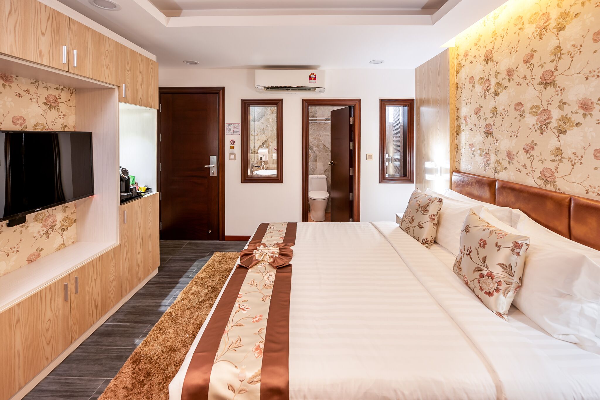 A hotel room with a large bed, wooden wardrobe, TV, and a bathroom visible through an open door.