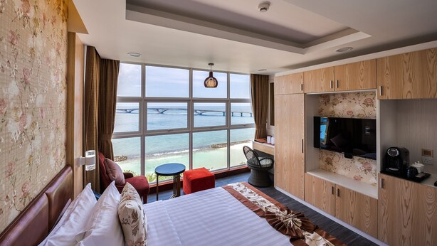 A hotel room with a large window, a bed, a TV, a small table, and a seating area. - Summer Beach Maldives (Malé)