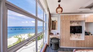 A modern room with large windows overlooking a beach and ocean, a wooden desk, a television, and a cozy seating area. - Summer Beach Maldives (Malé)