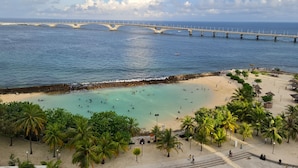 A beach with a bridge in the background, palm trees, and clear blue water. - Summer Beach Maldives (Malé)