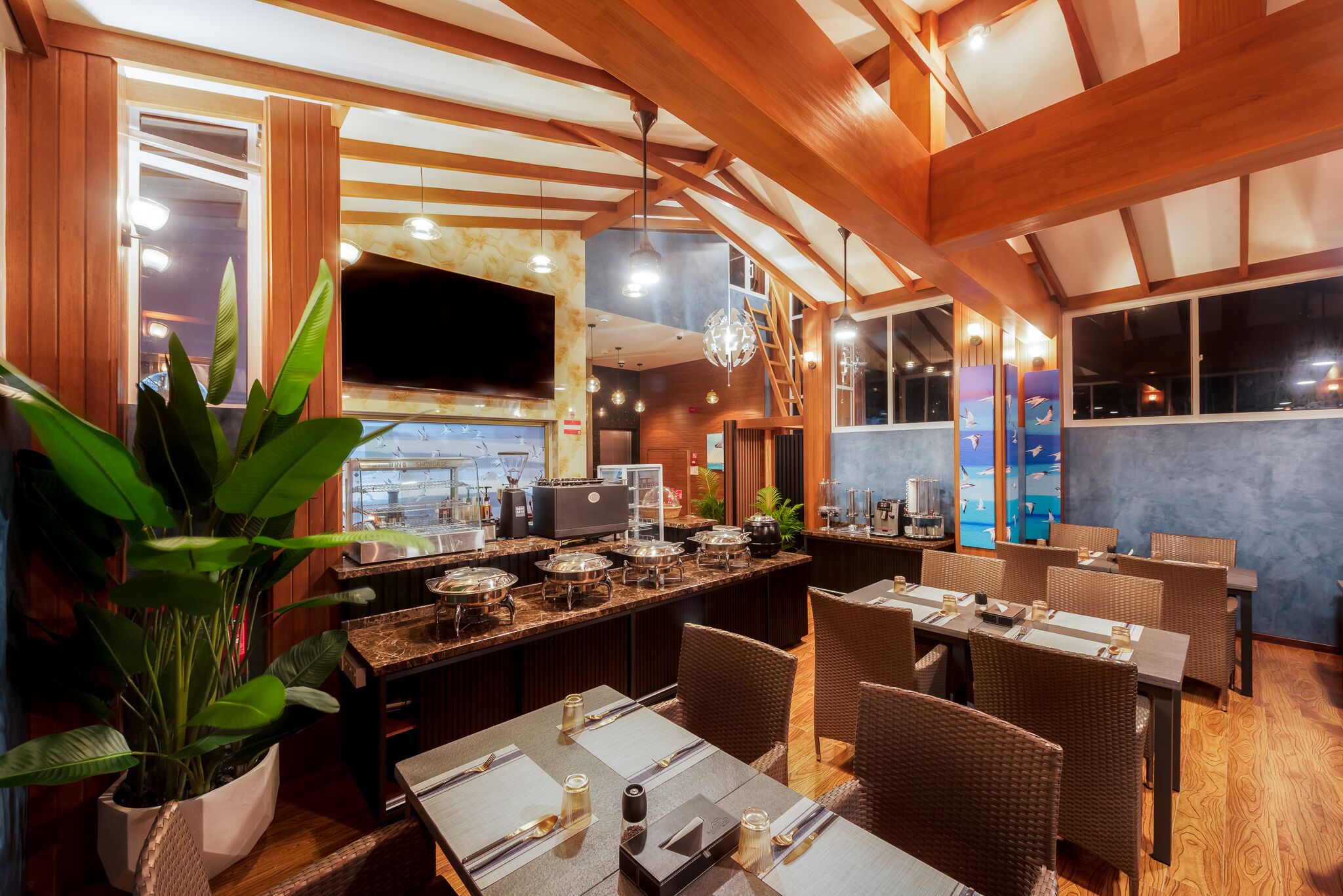 A restaurant with wooden beams, a large TV screen, and a buffet setup.
