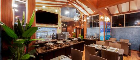 A restaurant with wooden beams, a large TV screen, and a buffet setup.