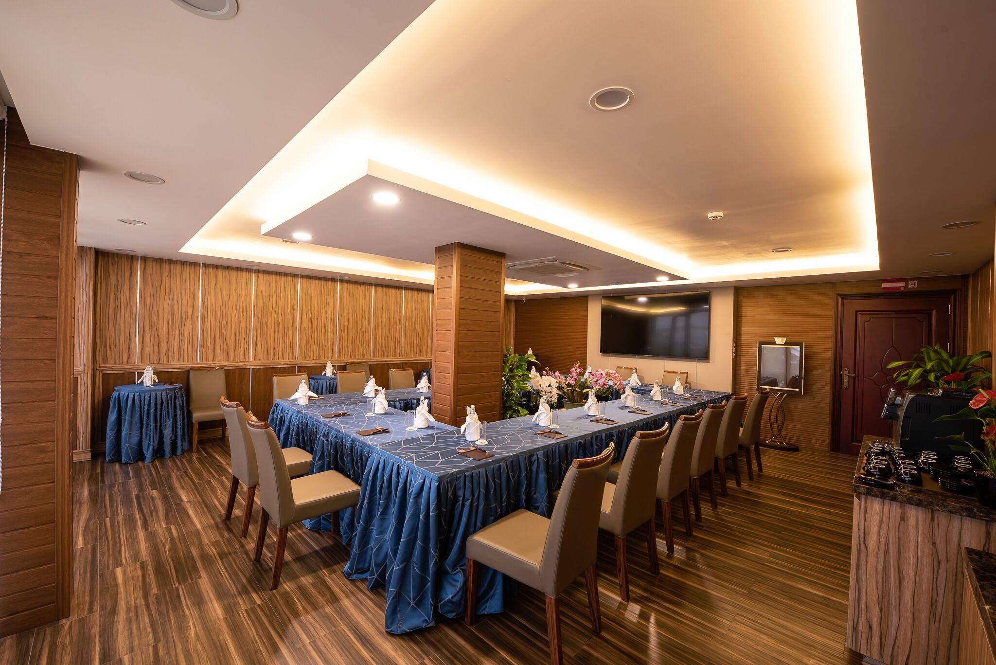 Un salón de conferencias con una larga mesa, sillas y una pantalla de televisión.