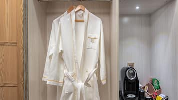 A robe hanging in a wooden closet with a shelf above containing a towel and a box labeled "Summer Beach Maldives."