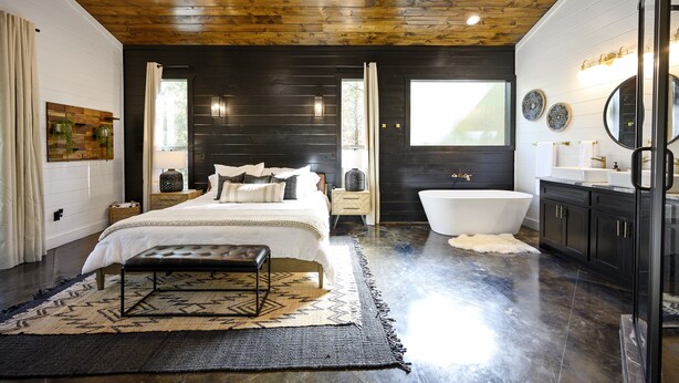 Een slaapkamer met een groot bed, een witte badkuip en een houten plafond.
