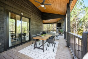 Une terrasse en bois avec une table et des chaises, un ventilateur de plafond et une cheminée en pierre.