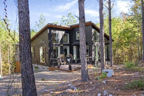 Une cabane en rondins moderne, dotée d’une terrasse et entourée d’arbres.