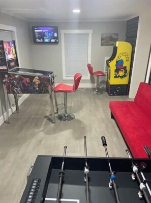 A room with a foosball table, two red chairs, a red sofa, and a TV mounted on the wall.